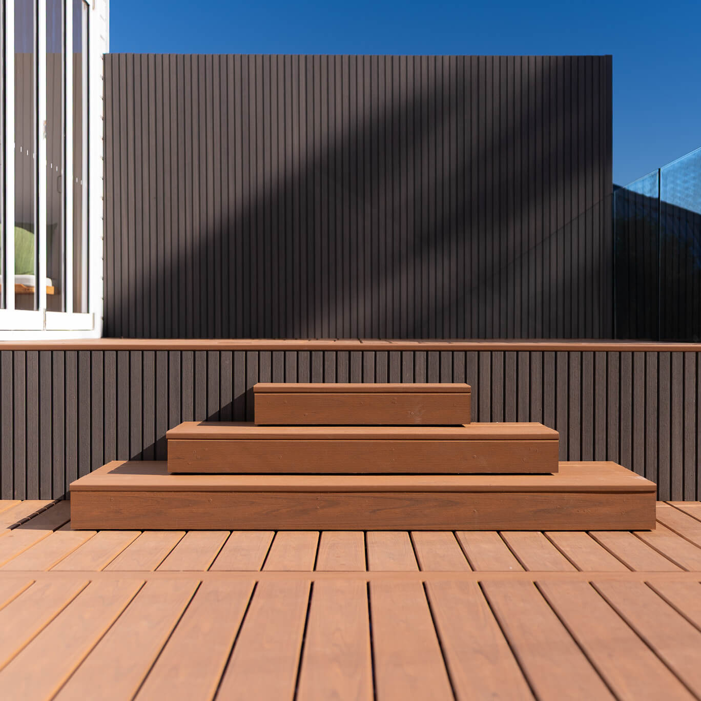 Tiered composite steps up to a raised Trex deck, with a NewTechWood Quick Panel cladding wall in Silver Grey and frameless glass, Dee Why