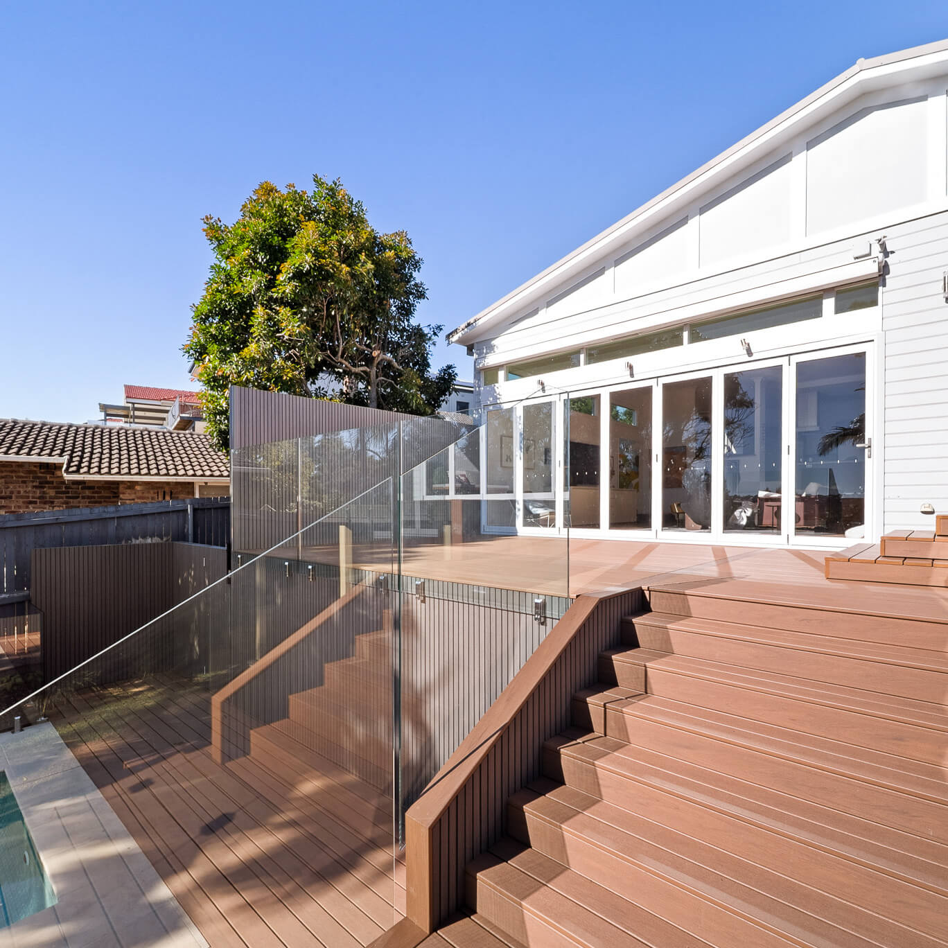 Two-level Trex Transcend Lineage deck in Hatteras with composite stairs, NewTechWood Quick Panel screens and cladding in Silver Grey, and frameless glass balustrades, Dee Why, by Kovacs Carpentry